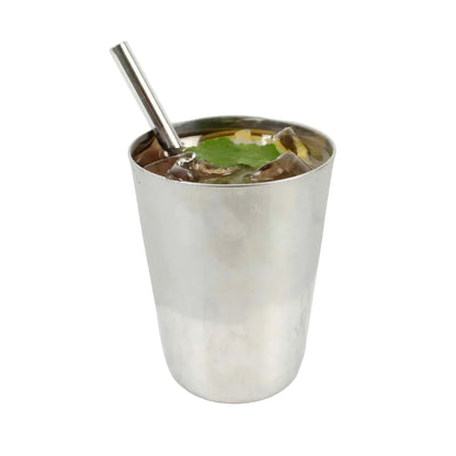 A stainless steel cocktail shaker filled with a dark drink, ice, and a green leaf, set on a light marble surface against a white background.