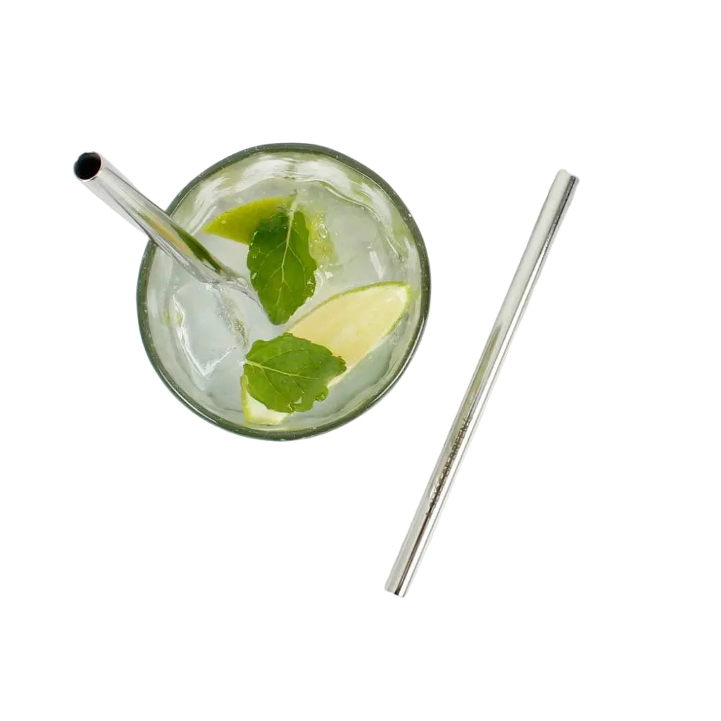 A clear glass with a metal straw containing a clear drink with mint leaves and a lime wedge, placed on a white marble surface next to a second metal straw.