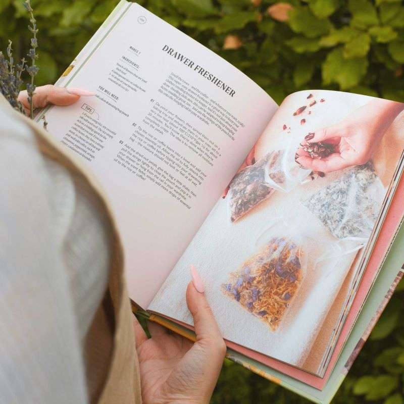 Person holding a book with recipes and images of food against a green outdoor background