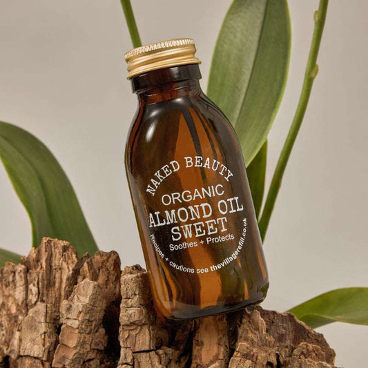 Amber glass bottle of Sweet Almond Oil ORGANIC with gold cap displayed on natural wood and green leaves background