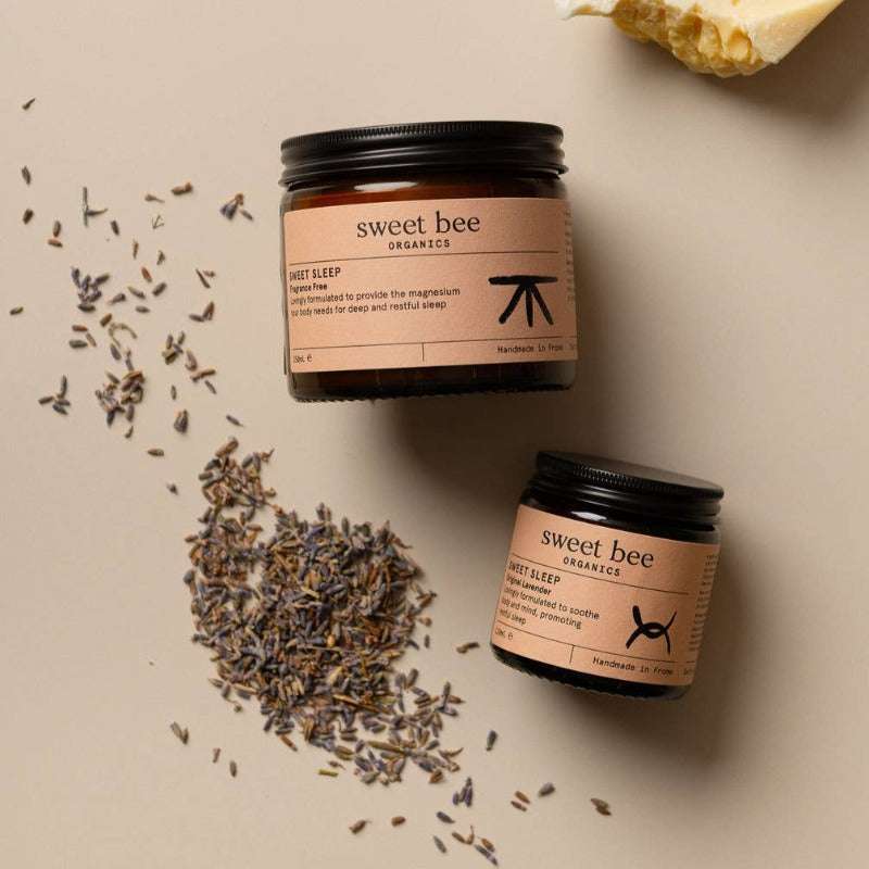 Two jars of 'sweet bee' products on a beige surface with lavender flowers.