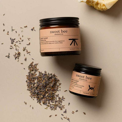 Two jars of 'sweet bee' products on a beige surface with lavender flowers.