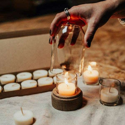 Hand holding a glass jar over a small candle on a rustic surface with other candles.