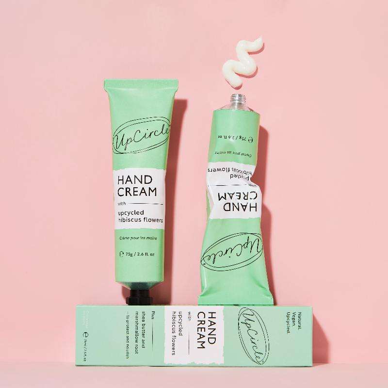 Two green tubes of hand cream with a box on a pink background