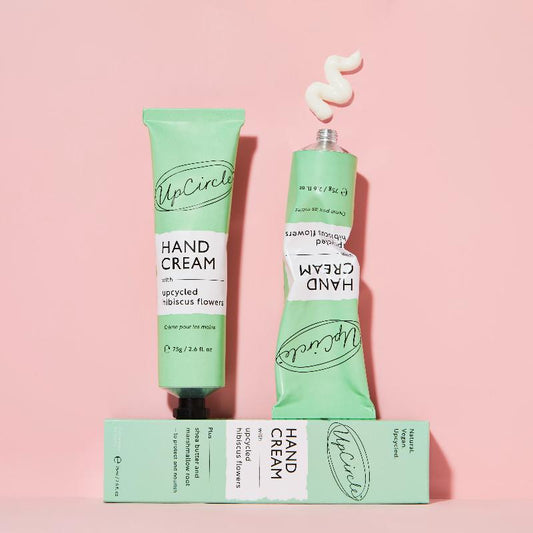 Two green tubes of hand cream with a box on a pink background