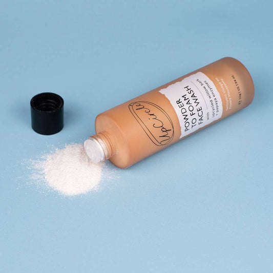 Bottle of powder face wash with a black cap on a blue background