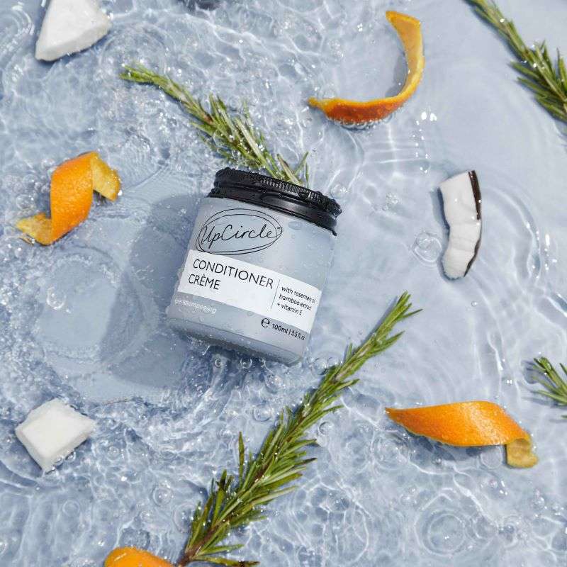 UpCircle Conditioner Crème jar on a textured surface with orange peels and rosemary leaves.