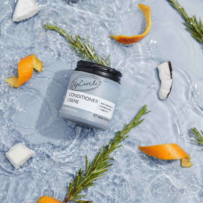 UpCircle Conditioner Crème jar on a textured surface with orange peels and rosemary leaves.