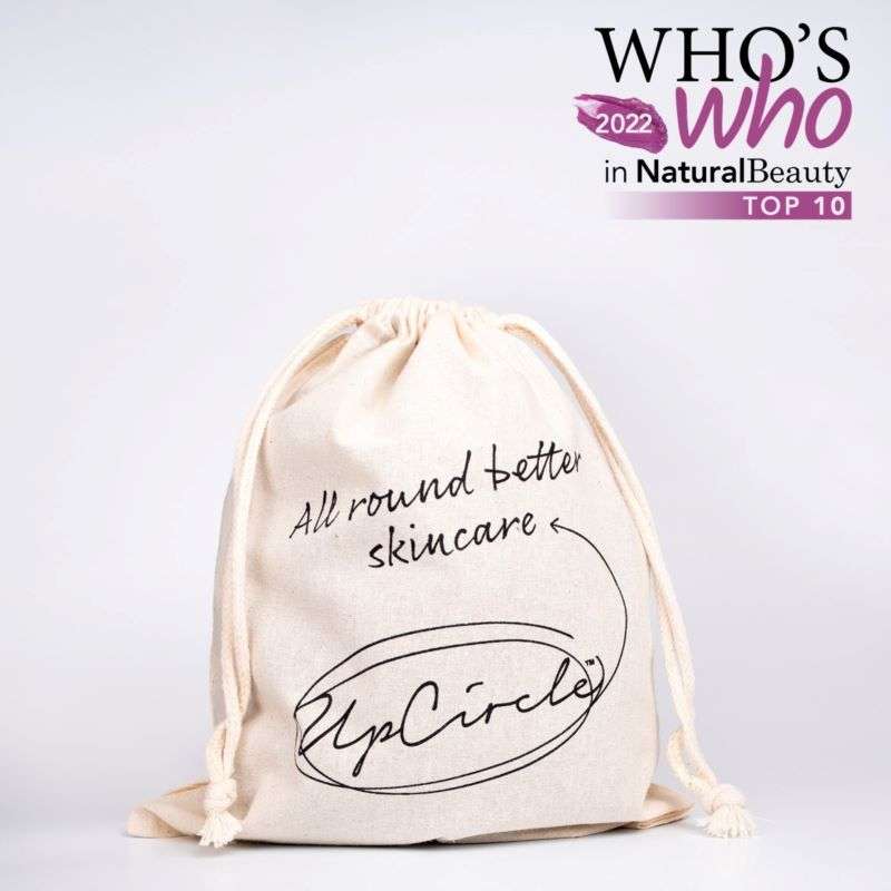 Beige drawstring bag with 'UpCircle' branding and text on a light gray background, featuring 'WHO'S WHO in Natural Beauty 2022 TOP 10' text.