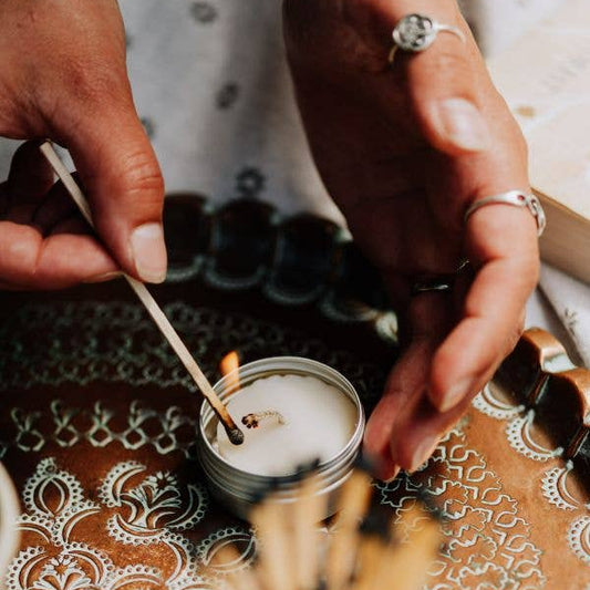 Person lighting a candle with a match on a decorative tablecloth.