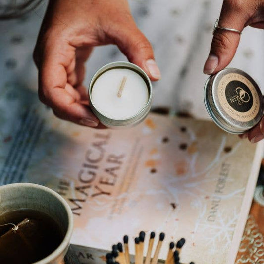 Two hands holding small candles over a book titled 'The Magical Year' with matches and a mug.