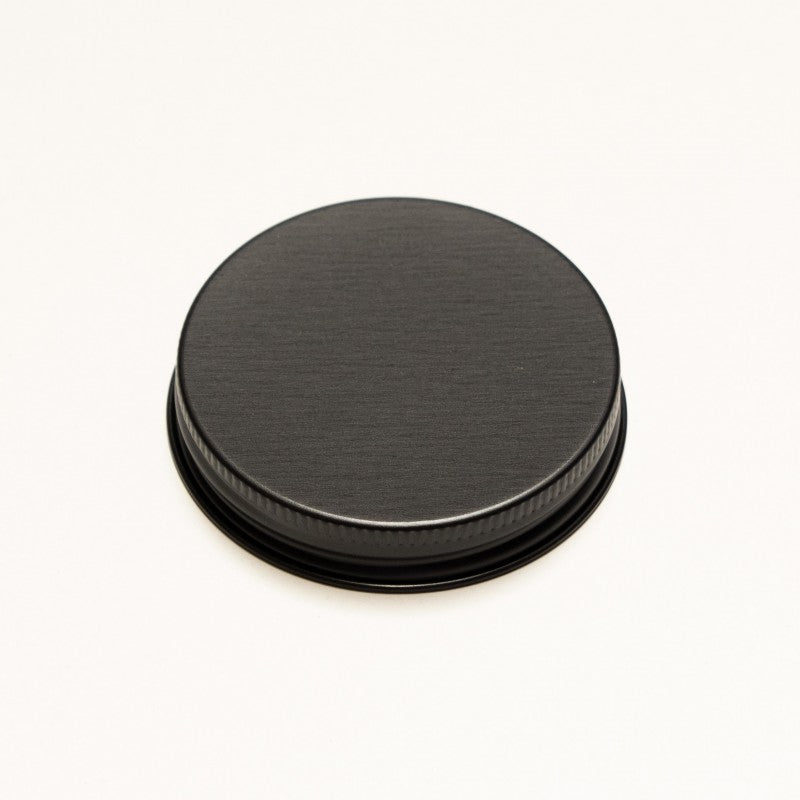 A round black metal screw-on lid with a brushed finish and a ribbed outer edge, shown on a plain white background.
