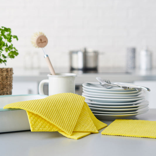 Yellow dishcloths on a kitchen counter with plates and utensils in the background.