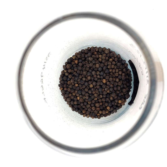 Glass container filled with black peppercorns on a white background