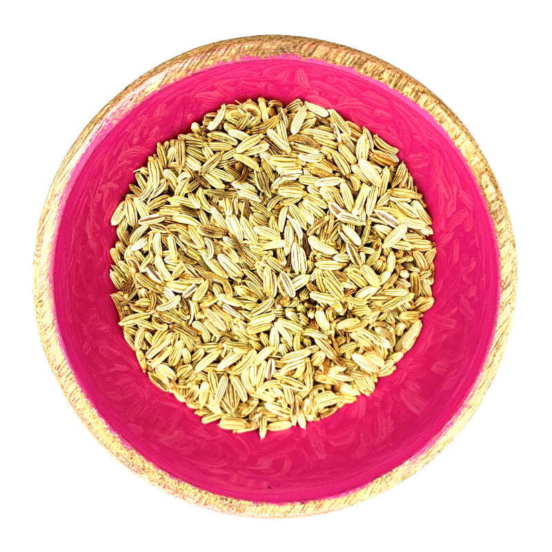 Pink bowl with gold rim filled with fennel seeds on a white background
