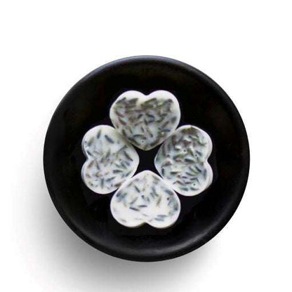 Heart-shaped white wax melts with dark specks on a black plate against a white background