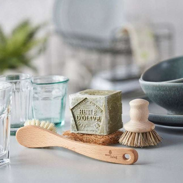 Bar of soap with wooden brush and scrubber on a surface with glasses and bowls in the background