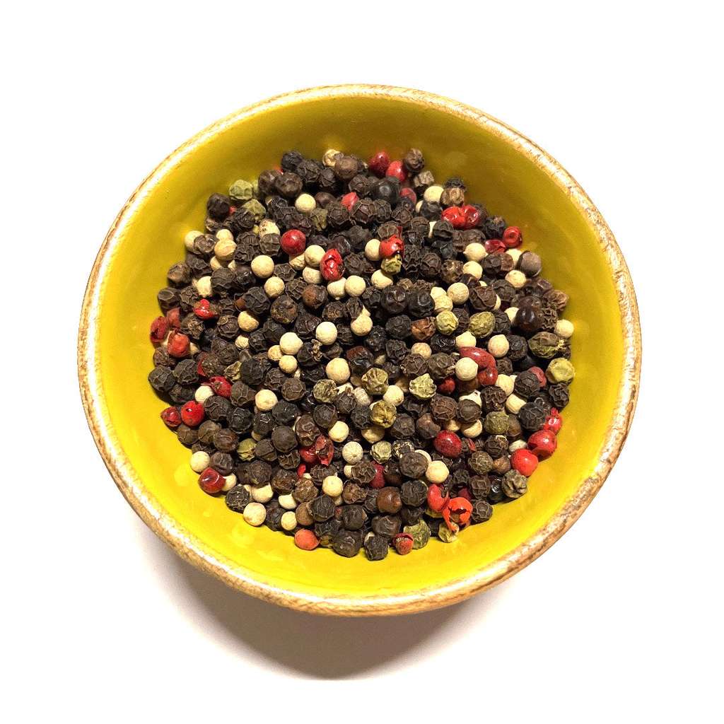 Yellow bowl filled with multicolored peppercorns on a white background