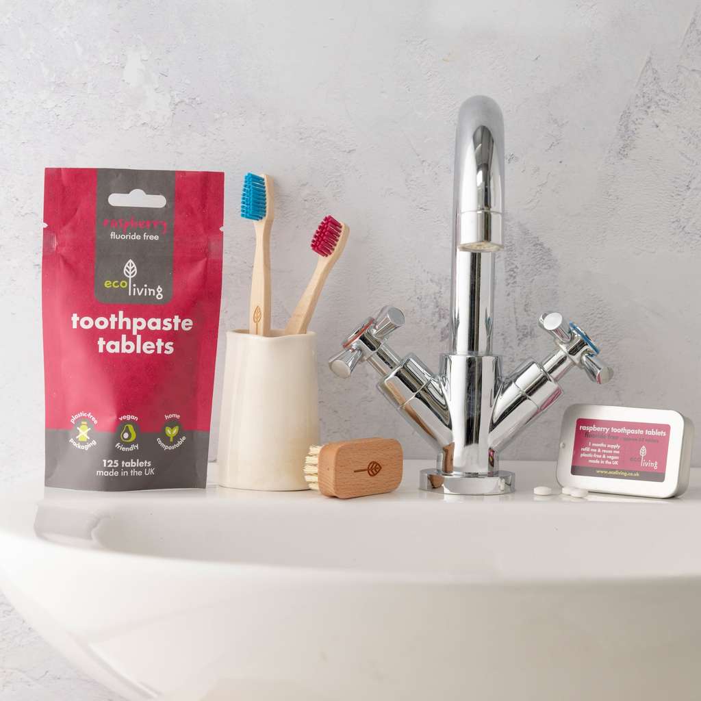 Eco-friendly bathroom setup with Toothpaste Tablets with FLOURIDE, bamboo toothbrushes, and natural cleaning brush near sink faucet